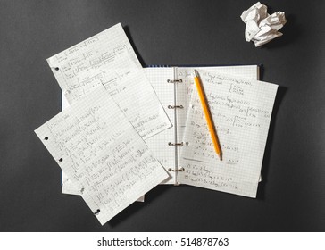 Solving A Mathematical Problem In A Notebook. Crumpled Piece Of Paper On Black Desk.