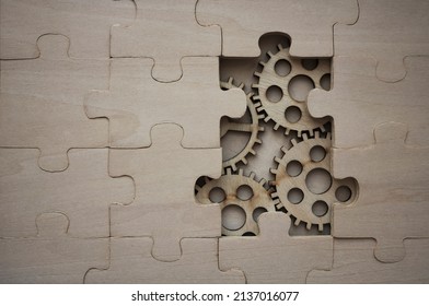 solving the problem concept - puzzles and cogwheels. wooden gears under the puzzle, the concept of moving to the next level. Cog wheels coming out from underneath a jigsaw puzzle