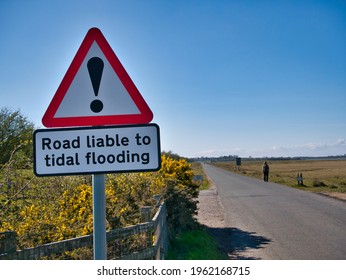 Solway, UK - Apr 15 2021: A Roadside Sign Warns That The Road Ahead May Be Flooded At High Tide. Taken On A Sunny Day With Blue Sky.