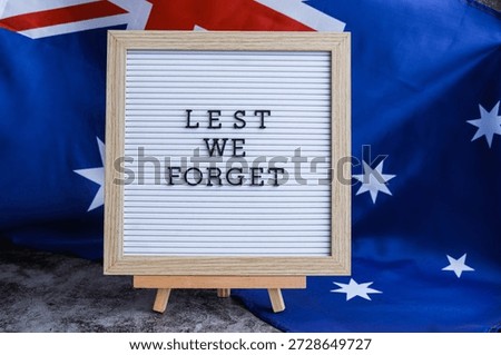 Somber Australian flag backdrop with text LEST WE FORGET on letter board. Respectful message for memorial ANZAC. Concept of remembrance and honor