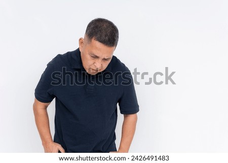 A somber middle aged man with a hunched posture appears downcast and regretful in a neutral space.
