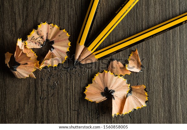 some black and yellow pencils and\
pencil shavings  placed on brown wood table surface texture\
