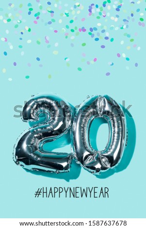 some confetti, two silvery number-shaped balloons forming the number 20, as the new year, and the hashtag happynewyear against a blue background