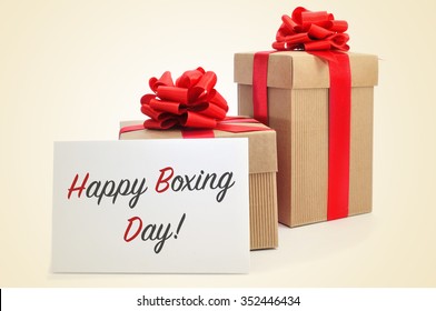 Some Gifts Tied With Red Ribbon And A Signboard With The Text Happy Boxing Day, On A Beige Background