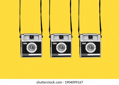 some gray and black retro film cameras, hanging from their strips, on a yellow background