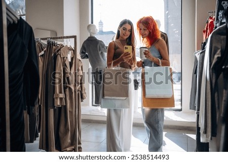 Some information in smartphone, reading. Two female friends are in the retail store, choosing clothes, shopping.