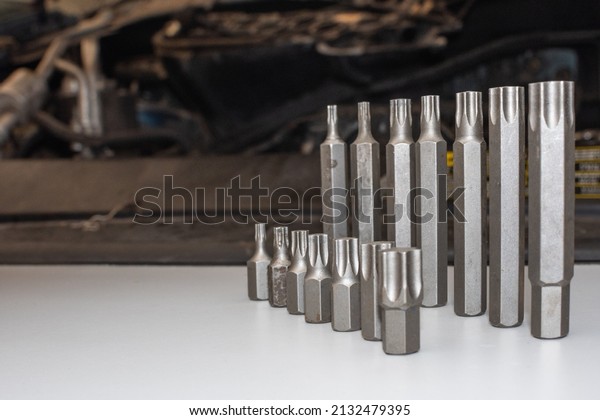Some mechanic tools on a white table. in the\
background are a car\
engine