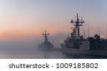 Some navy frigates and destroyers in port during a cold and foggy morning in a naval base. A fog bank between ships in port during a cold sunrise.