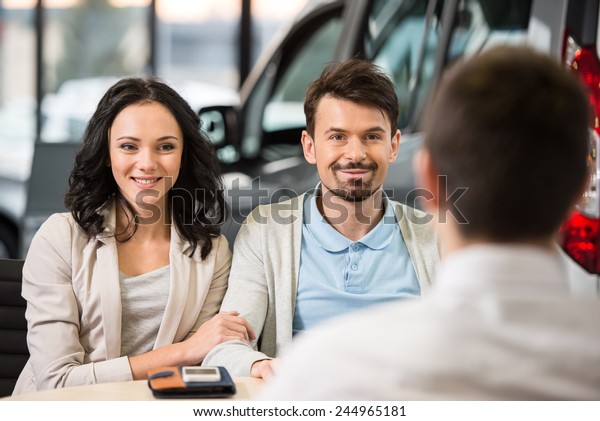 Some paperwork before buying a car.\
Young car salesman talking to a couple in auto\
salon.