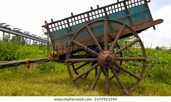 Some Photos of Old indian wooden bullock cart in\
green farm. Vintage style wooden bullock cart in rusty brown colour\
with pleasant sky.