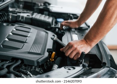 Some problems under the hood. Man in uniform is working in the autosalon at daytime.