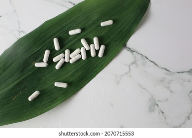 Some White Pills On A Big Rgeen Leaf On A White Marmol Background