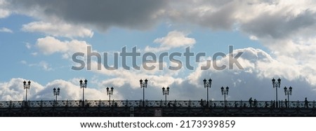 Somebody on the bridge. Autumn sunset. People are as a black silhouettes. Architecture. Picture on the top. Blue and white sky with clouds. Free space for your message