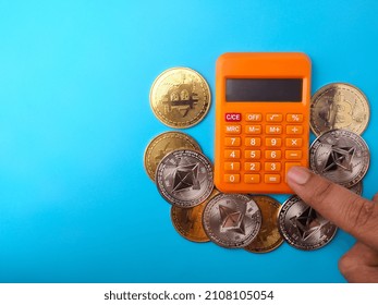 Someone Is Calculating Using A Calculator With Digital Coins On A Blue Background With Copy Space.