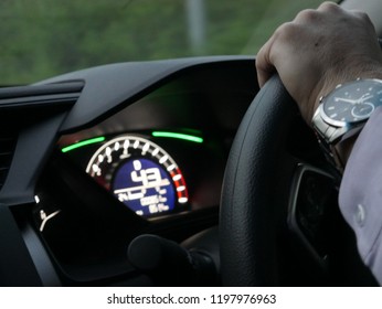 Someone driving the car and control his car by steering wheel looking at speed o meter to see the speed.