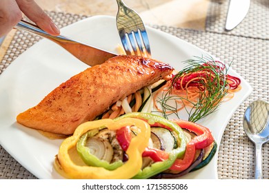 Someone Eating Salmon Filet And Vegetables With A Fork And Knife, On A White Plate, Restaurant Meal, Healthy Food