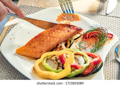 Someone Eating Salmon Filet And Vegetables With A Fork And Knife, On A White Plate, Restaurant Meal, Healthy Food