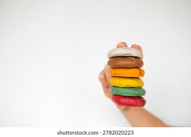 Someone holding a stack of donuts with different colors on them.