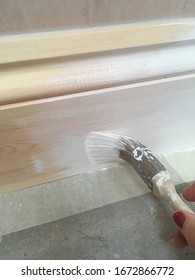 Someone Painting White Primer Onto A New Wood Skirting Board Above Concrete Floor