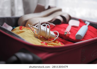 Someone is preparing a suitcase with various clothes and travel items.
