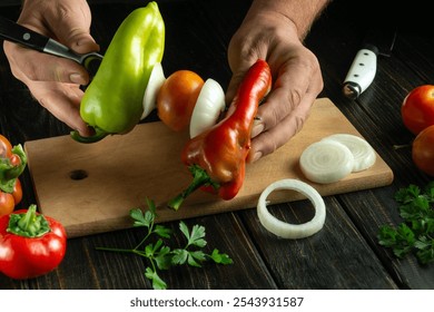 Someone skillfully cuts and threads colorful peppers, tomatoes, and onions onto skewer. Fresh herbs and additional vegetables surround the wooden cutting board, adding to the preparation atmosphere. - Powered by Shutterstock