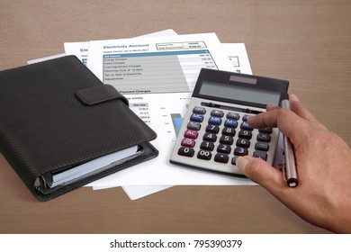 Someone Using Calculator To Summarize Amount Of Electricity Cost From All Bills On Wooden Desk.