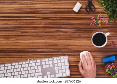 Someone is using computer keyboard and mouse next to modern black smartphone with empty screen, cup of black coffee and plant od dark wooden office desk. - Powered by Shutterstock