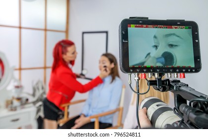 Someone is video recording when a make-up artist is doing her work and she is applying some powder on her client's face.