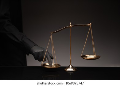 Someone wearing black shirt pressing the imbalance scale on black glass desktop and black background, cheating  in a lawyer's office, Concept of injustice, espionage, partiality, law. - Shutterstock ID 1069895747