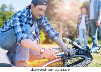 Something gone wrong. Selective focus on a smart mindful father concentrating on a bicycle while fixing it with his son and father watching him in the background.