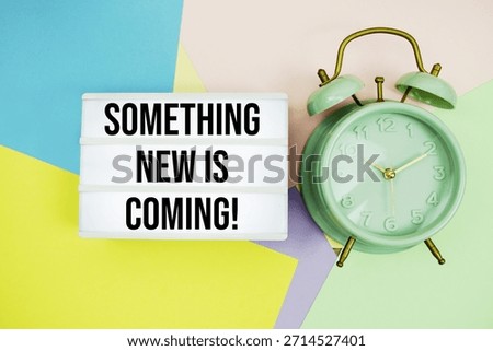 Something New Is Coming! text in lightbox with alarm clock on pastel background