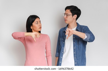 Something Went Wrong. Asian Confused Couple Looking At Each Other With Their Thumbs Down, Grey Background