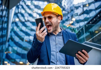 Something is wrong on building site. Angry construction engineer yelling on head of the construction site while talking with him via mobile phone. Construction concept
