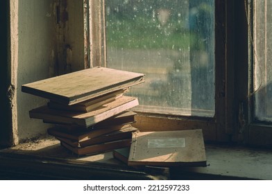 Somewhere in an abandoned house, old dusty books and ledgers are lying on a dirty windowsill, the light of the evening sun is coming through the dirty window - Shutterstock ID 2212597233