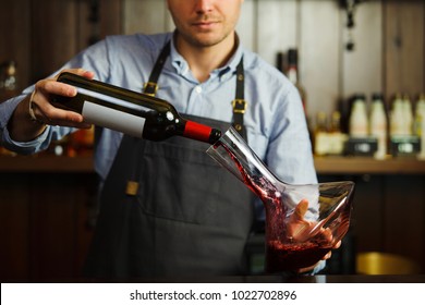 Sommelier pouring wine into glass from decanter. Male waiter