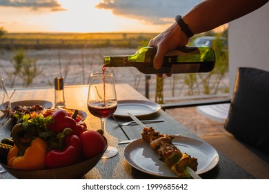 Sommelier Pours Wine Into A Glass At Sunset. Red Wine With Dinner On The Summer Terrace. Meat With Red Wine In Summer. Picnic With Wine And Meat On The Gazebo. Picnic At Home With Meat . Food Day