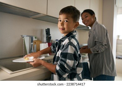 A son with cute eyes washing dishes near the mom at home apartment - Powered by Shutterstock