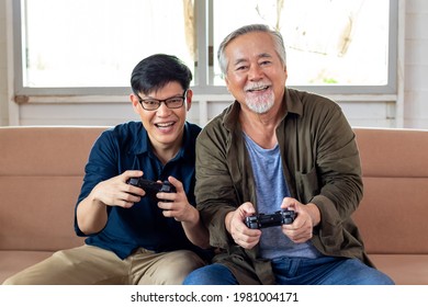 Son and dad enjoy playing video game together sitting on sofa in cozy home, smiling and laughing together. Senior Asian man having fun time with Young Asian man. Father's day and happy family concept. - Powered by Shutterstock