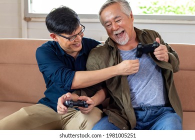 Son and dad fight for gamepad in cozy home, smiling and laughing together. Senior Asian man challenge with Young Asian man gamer. Father's day and happy family concept. - Powered by Shutterstock