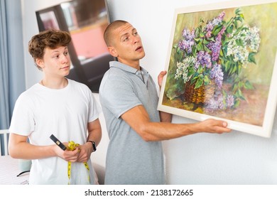 Son And Dad Hanging Picture Of Lilac On Wall. Son Holding Hammer In Hands.