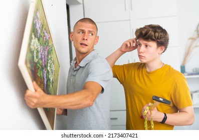 Son And Dad Hanging Picture Of Lilac On Wall. Son Holding Hammer In Hands.