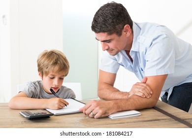 Son doing homework while father standing by at table in house - Powered by Shutterstock