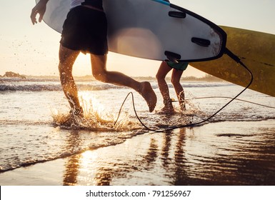 Son and father surfers run in ocean waves with long boards. Close up splashes and legs image - Powered by Shutterstock