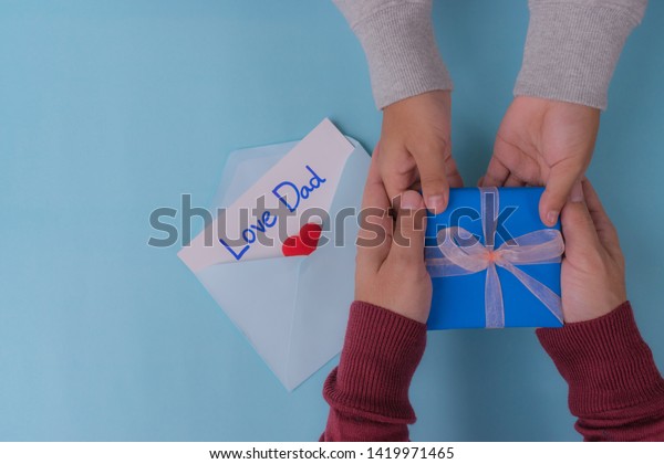 Son\
gives a gift to dad. Fathers day concept. Blue paper envelope with\
text \