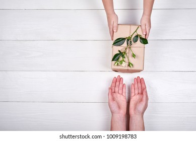 Son Giving Gift Box With Flowers To Mum, Top View. Holidays, Present, Childhood Concept. Close Up Of Child And Mother Hands With Gift Box On White Background. Mothers Day, Womans Day (March 8)