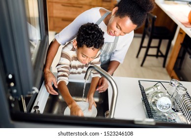 Son is helping mother in the Kitchen, Washing Dishes. African American family.