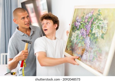 Son Helps Father To Hang The Painting On The Wall Of The House