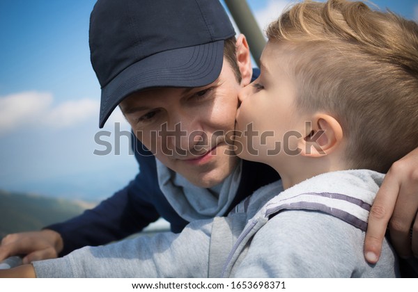 Son kissing\
father on the cheek in nature.\

