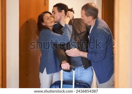 Son leaving parents concept. Son with suitcase hugging parents before moving out