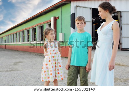 Son, mother and little daughter stand near long stall for cows at farm.